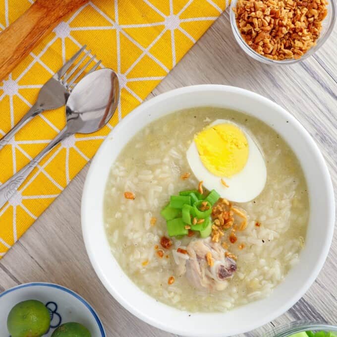 鸡肉Arroz Caldo装在白色的碗里，上面有煮鸡蛋，葱和炸蒜块