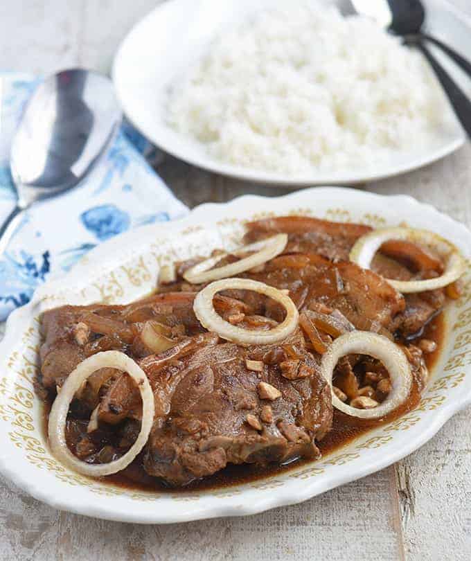 猪肉小酒馆在服务盛肉盘上装饰着洋葱圈，侧面有一盘蒸米饭